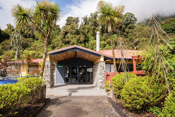 A building with a stone facade, a red roof, and a wooden entrance canopy. - Haka House Franz Josef (Franz Josef Glacier)