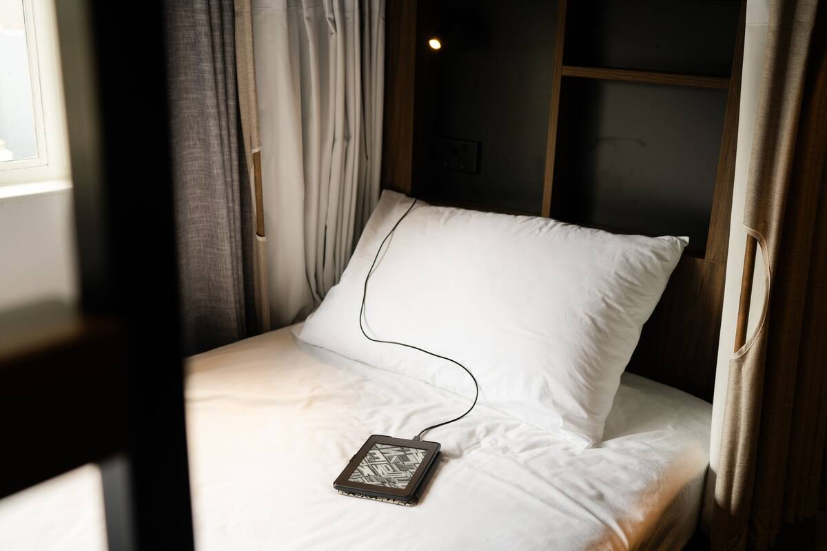 A bed with a white pillow and a tablet connected to it.