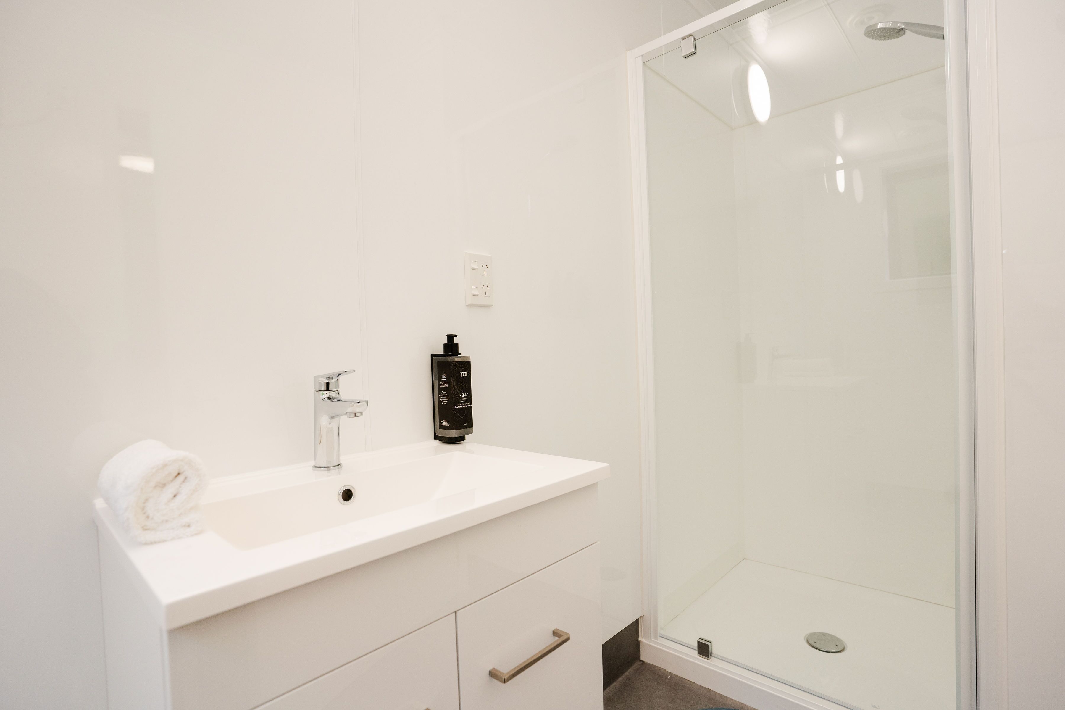 A modern bathroom with a white sink, a black soap dispenser, and a glass shower enclosure.