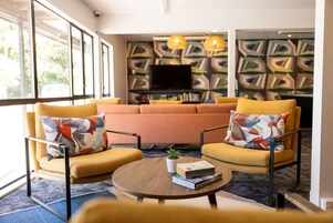 A living room with yellow armchairs, a round coffee table, and a flat-screen TV against a geometric patterned wall.