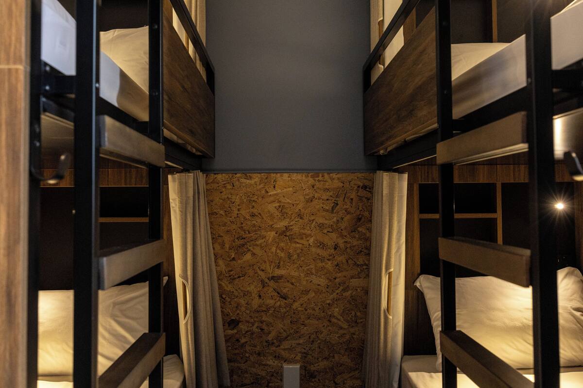 Una habitación estrecha con literas, paredes de madera y un ventanal pequeño.