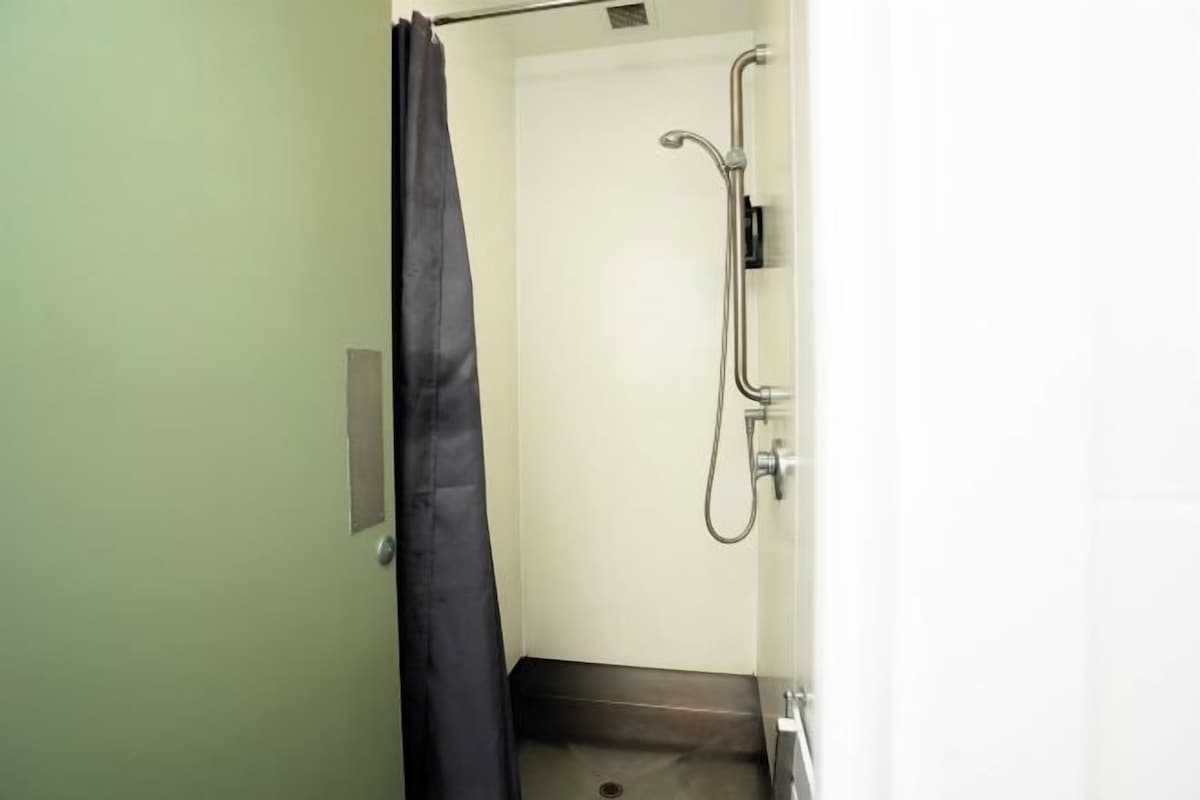 A small, narrow bathroom with a shower, a towel rack, and a door.