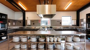 A modern kitchen with stainless steel appliances, a central island with stacked plates, and a wooden ceiling. - Haka House Rotorua (Rotorua)