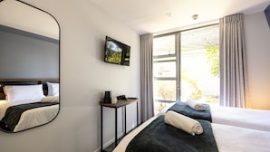 A hotel room with a large bed, a smaller bed, a TV mounted on the wall, a desk with a phone and a coffee maker, and a window with curtains. - Haka House Rotorua (Rotorua)
