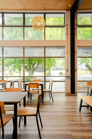 A spacious room with large windows, wooden flooring, and orange chairs. - Haka House Rotorua (Rotorua)