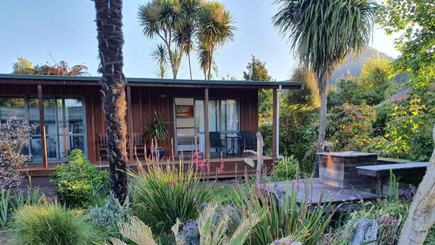 A modern house with a wooden deck, surrounded by lush greenery and tropical plants. - Off The Beaten Trail Accommodation & Bike Tours (Murchison)