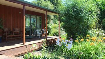 Una terraza de madera con mobiliario exterior, rodeada de abundante vegetación y plantas con flores.