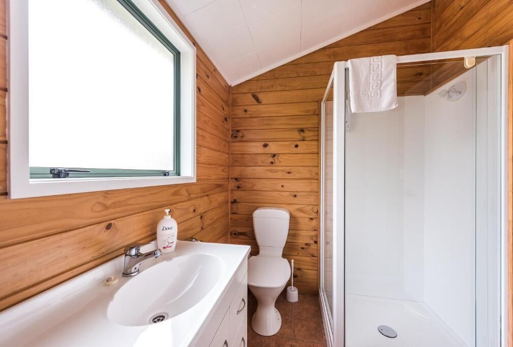 A bathroom with wooden walls, a white sink, a toilet, and a shower.