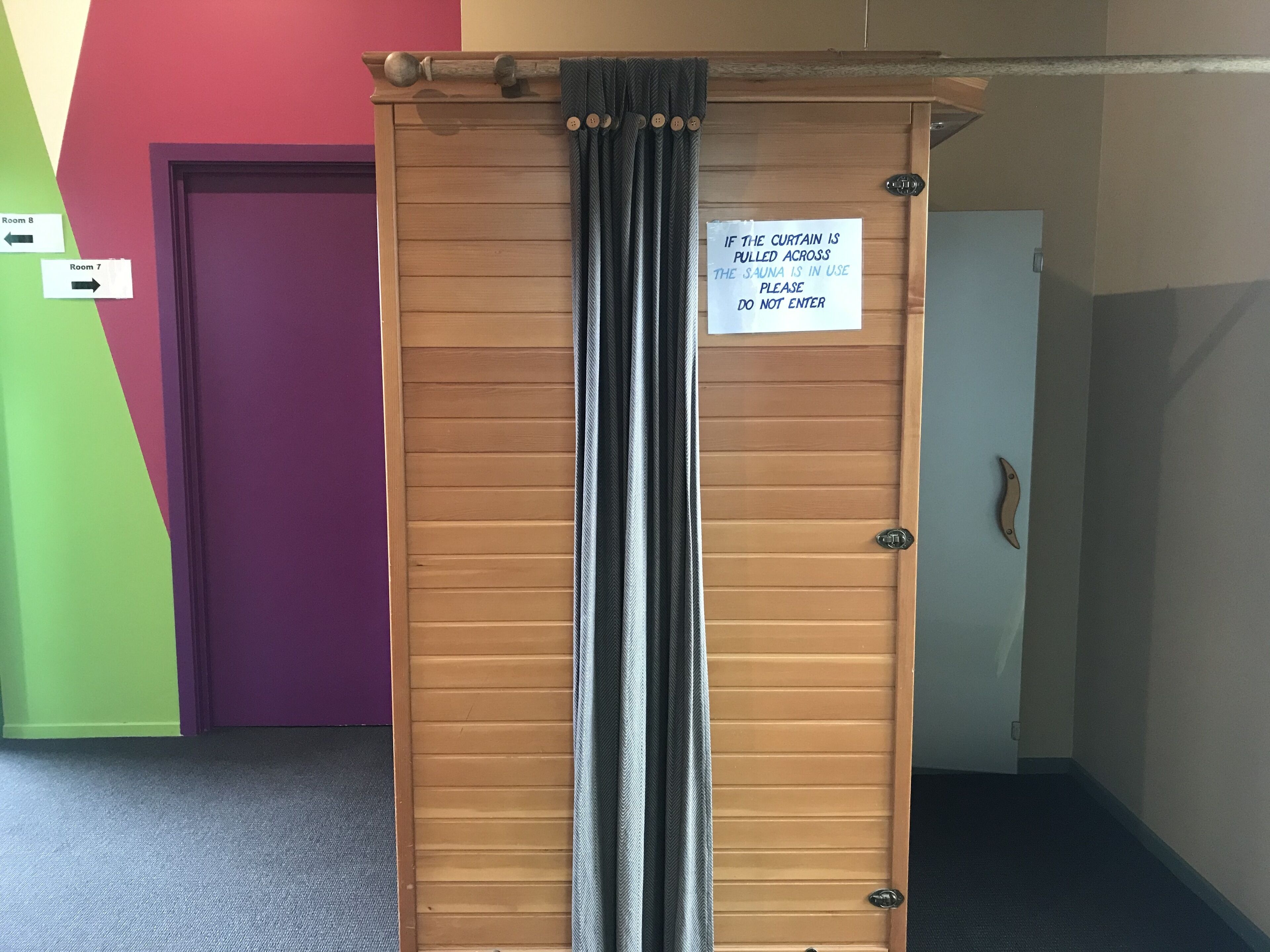 A room with a sliding door, a sign indicating the use of the sauna, and directional signs to Room 7 and Room 8.
