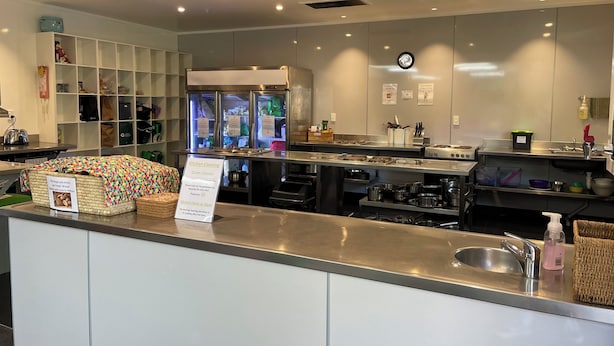A modern kitchen with stainless steel appliances, a freezer, and a sign indicating kitchen cleaning times. - YHA Nelson - Backpackers (Nelson)