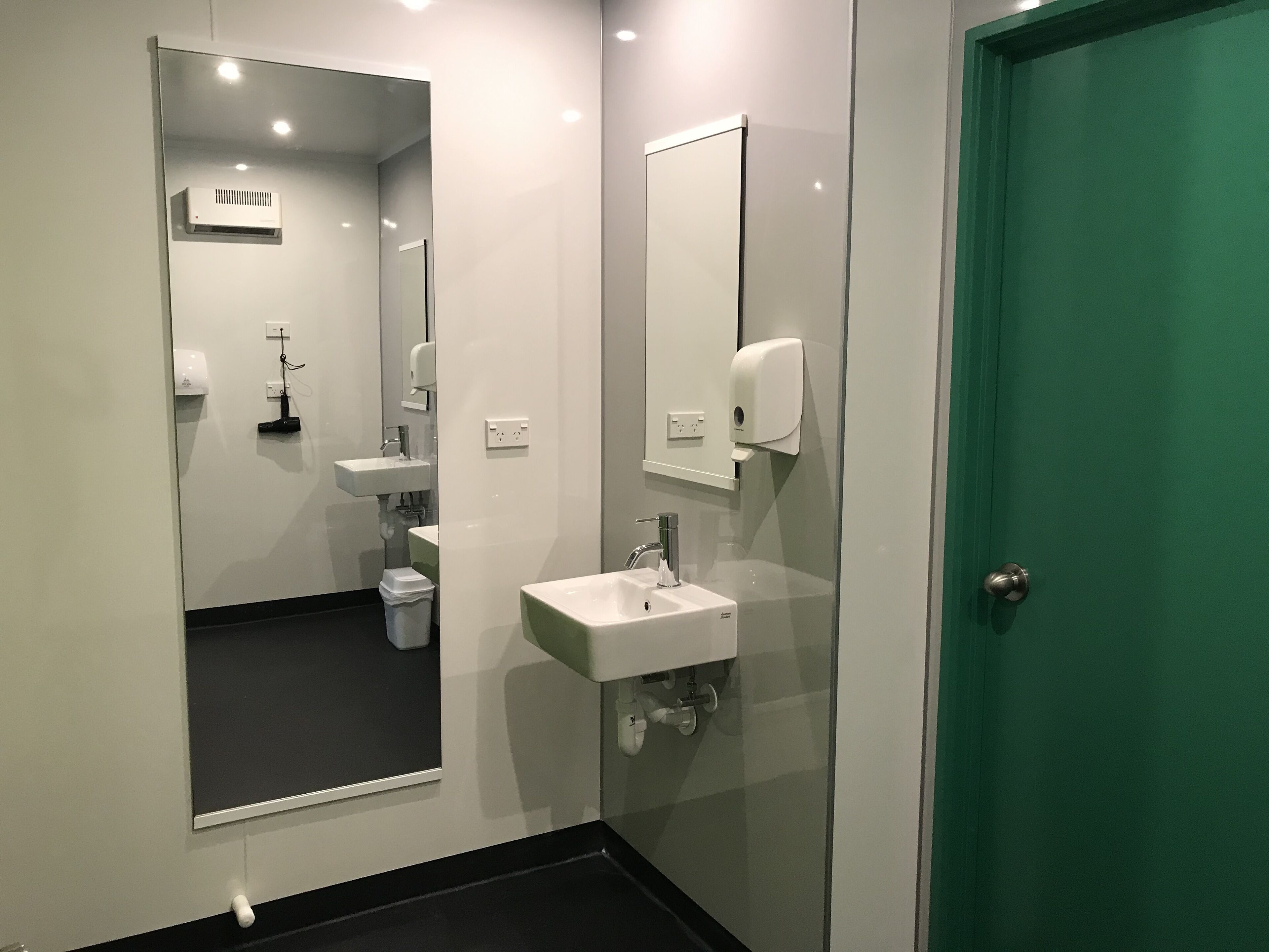 A modern bathroom with a large mirror, a sink, a toilet, and a green door.
