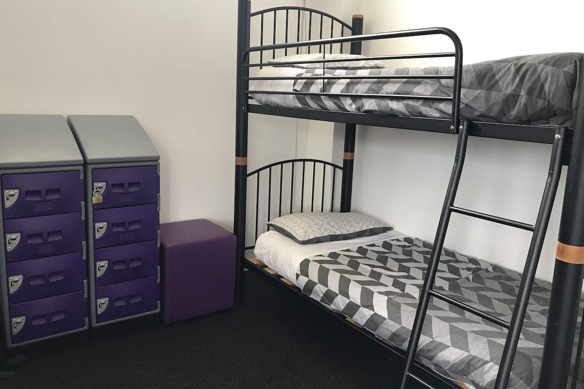 A bunk bed with a mattress and pillows, a purple storage unit with multiple drawers, and a small purple stool.