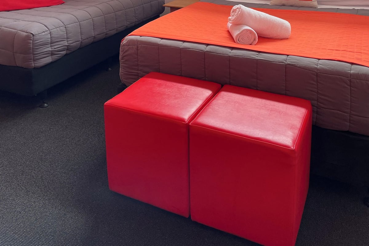 A hotel room with a bed, a sofa, and a red ottoman.