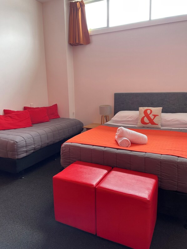 A hotel room with a bed, a sofa, and a red ottoman. - YHA Nelson - Backpackers (Nelson)