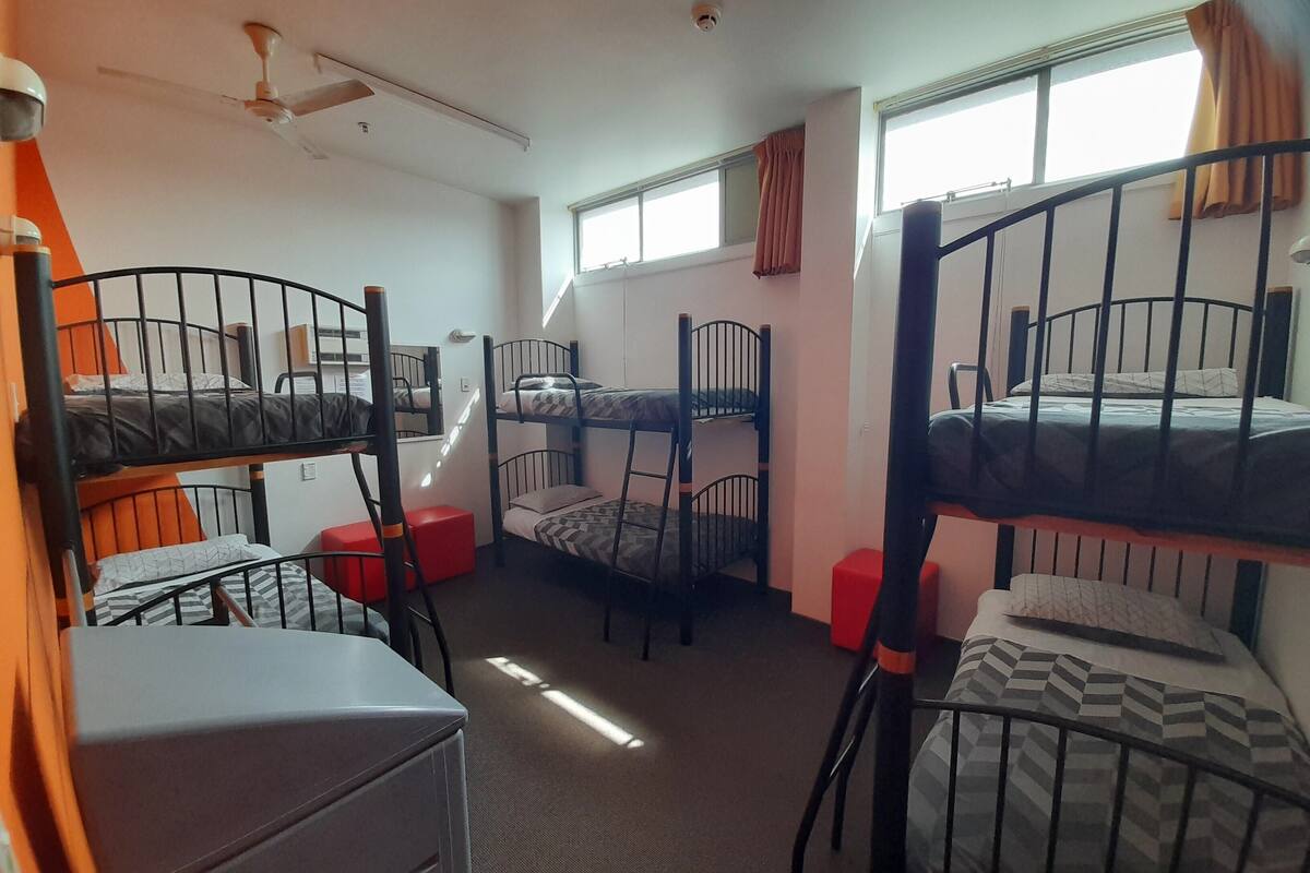 A dormitory room with bunk beds, a desk, and a chair.