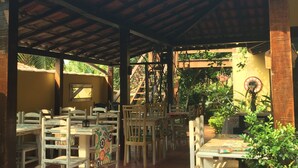 An outdoor patio with wooden tables and chairs, surrounded by greenery and a tiled floor. - Bella Geriba Suites (Búzios)