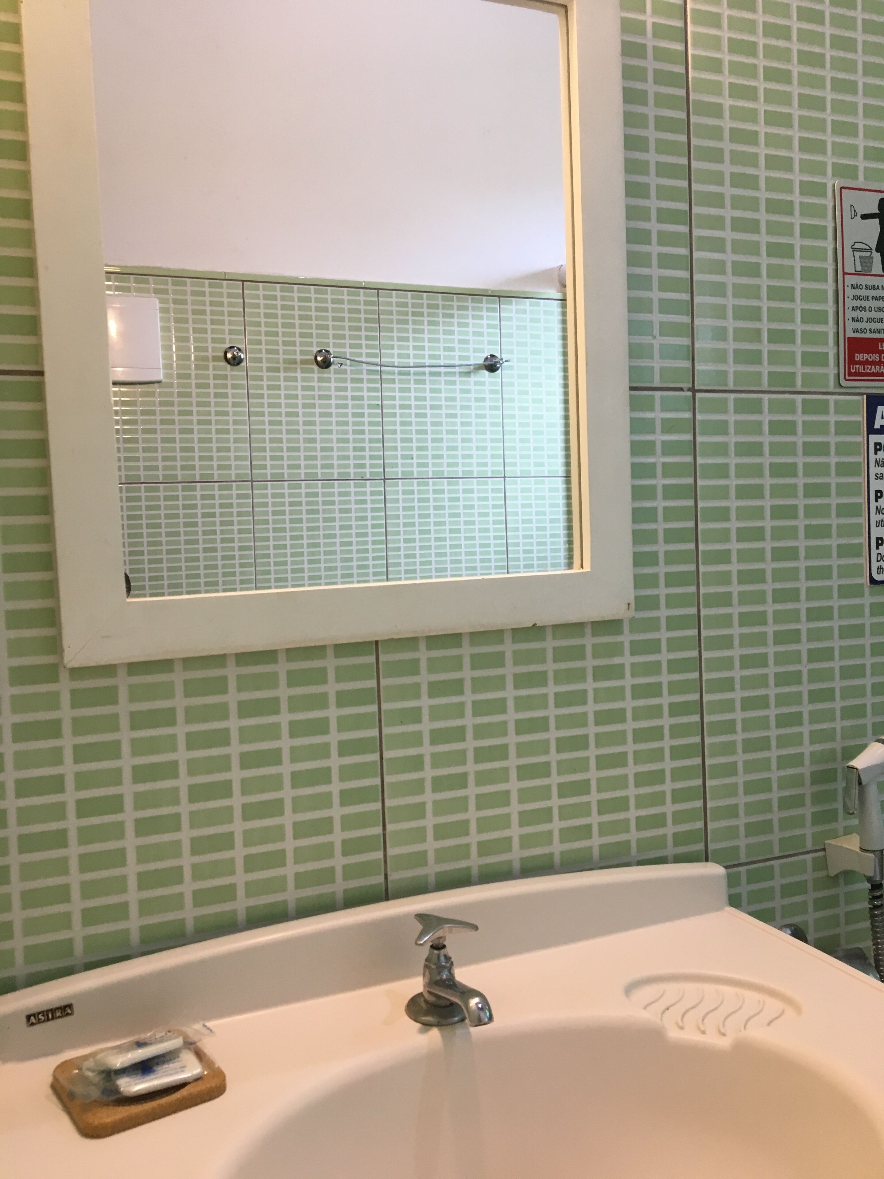 A bathroom with a white sink, a mirror above it, and green tiled walls.
