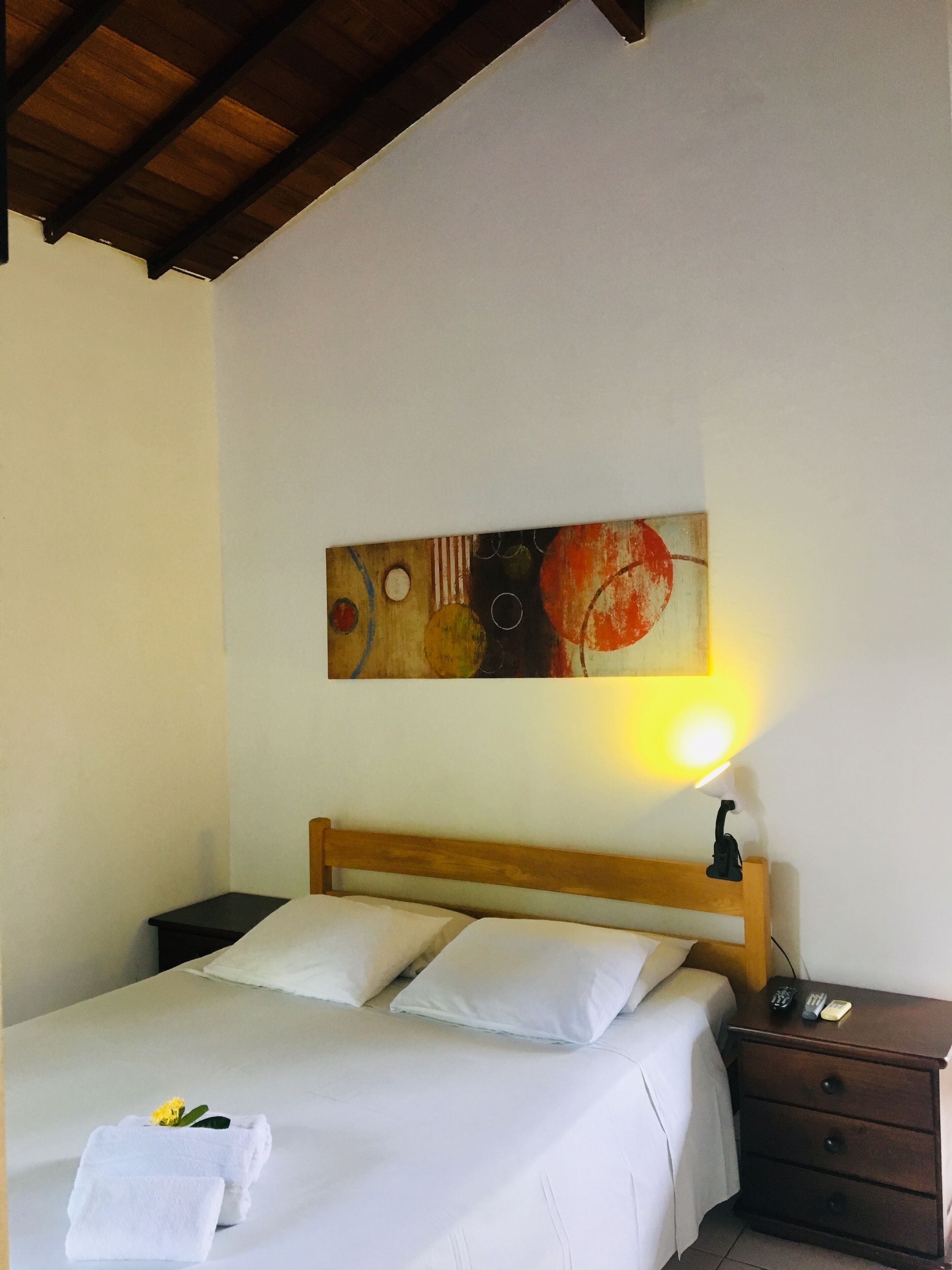A hotel room with a bed, a nightstand, a lamp, and a painting on the wall.