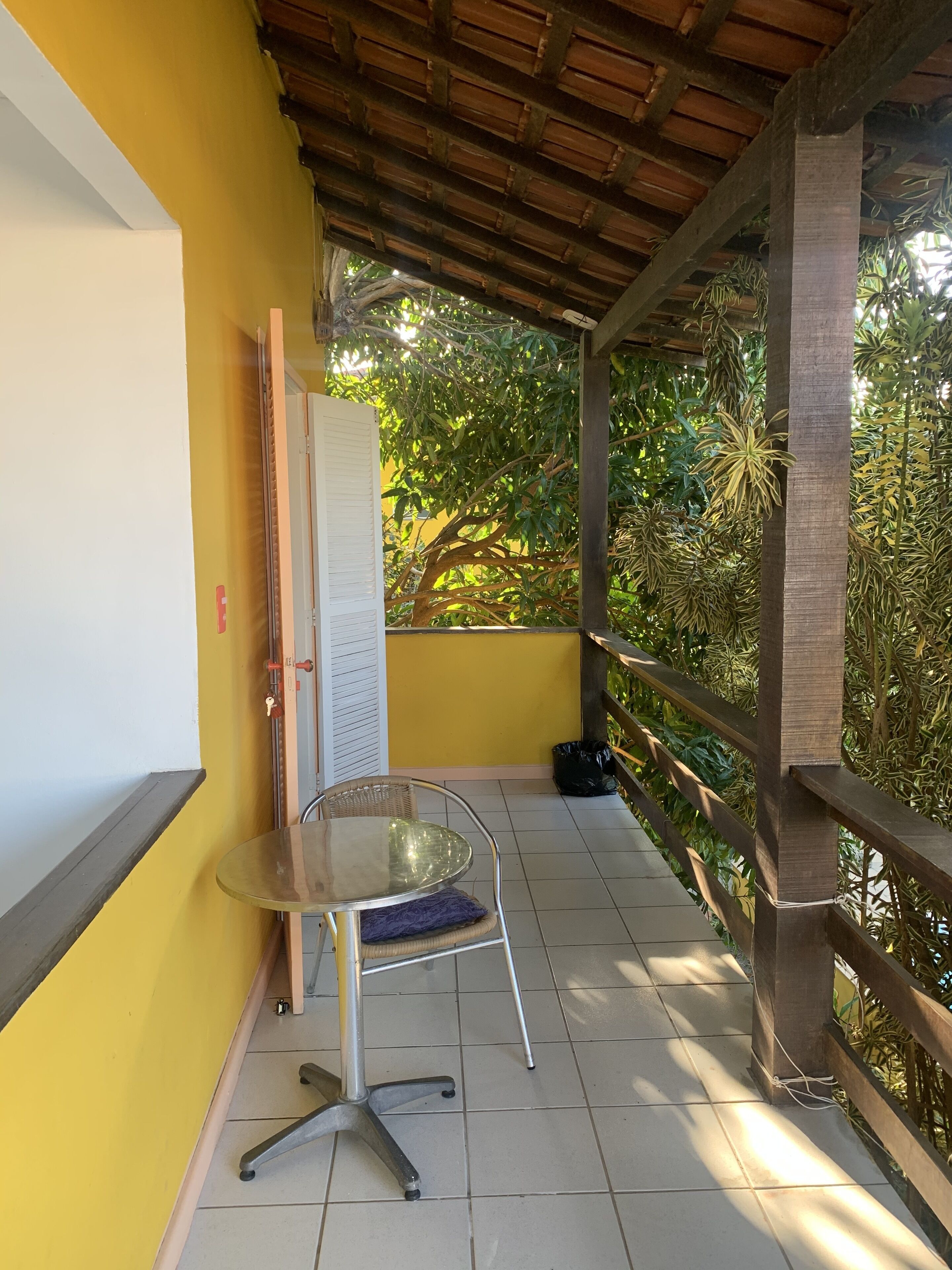A balcony with a table and chair, yellow walls, and a view of greenery.