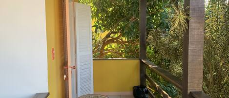 A balcony with a table and chair, yellow walls, and a view of greenery.