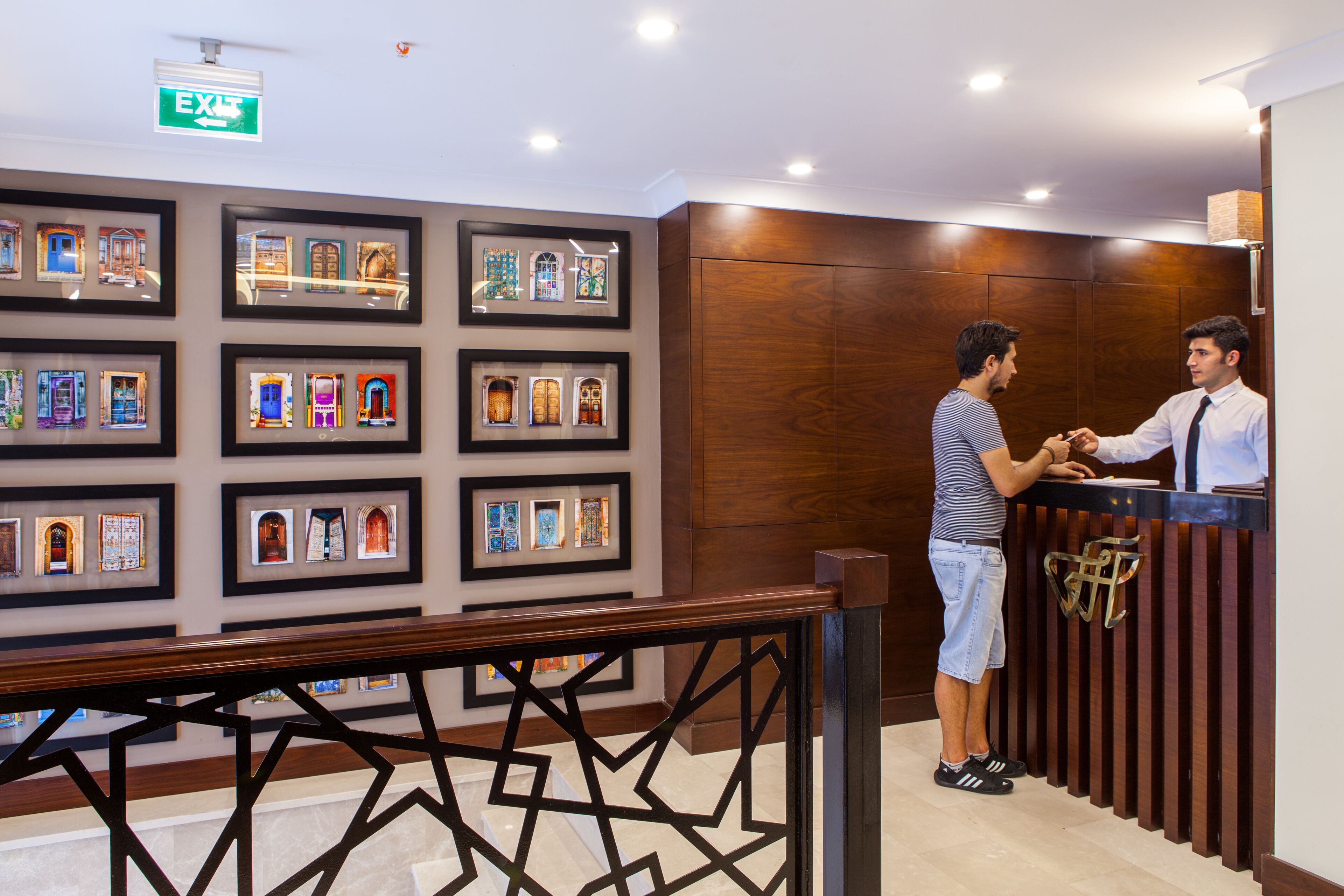 A reception desk with framed pictures on the wall, a wooden panel wall, and a sign indicating an exit.