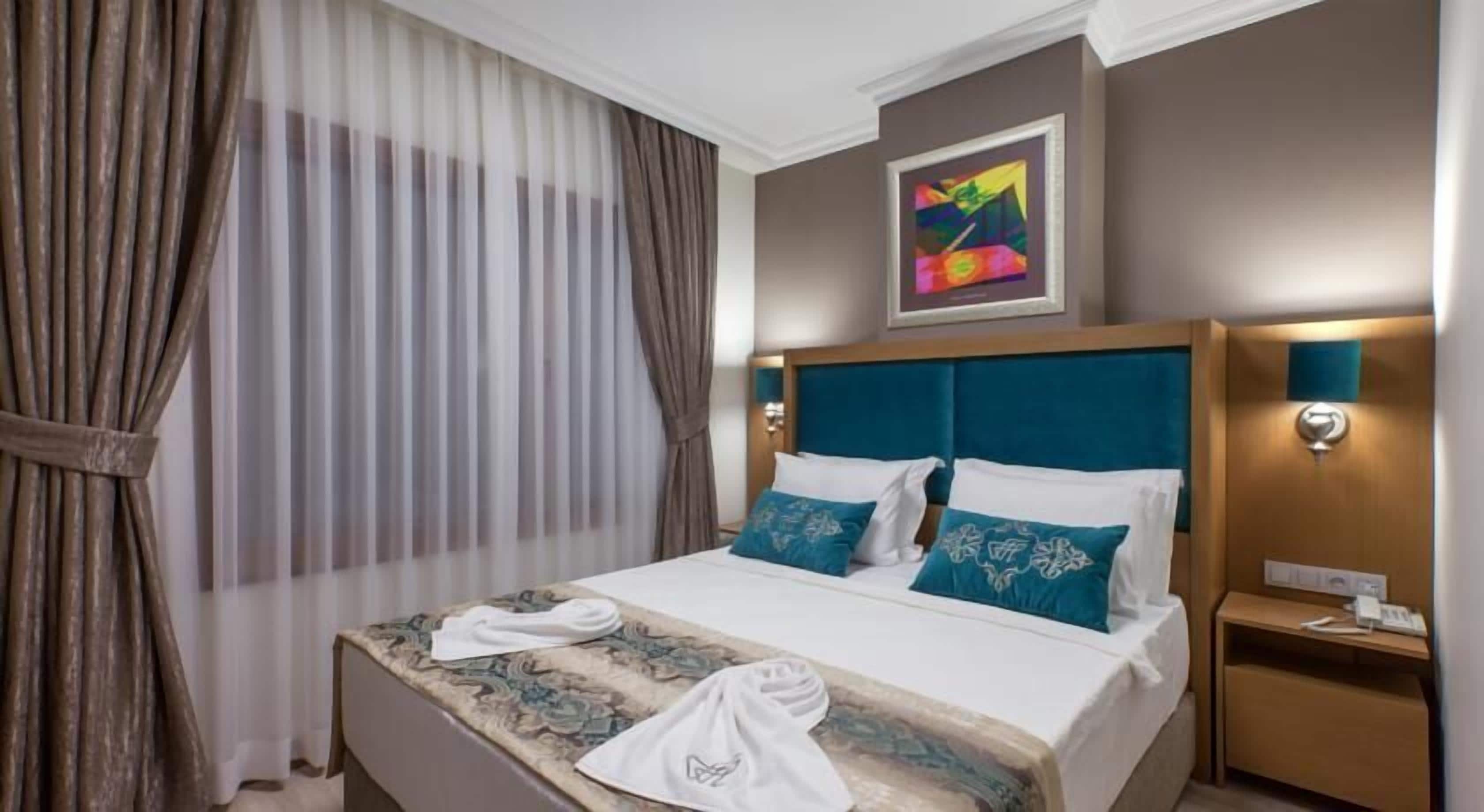 Una habitación de hotel con cama, cortinas, un cuadro y una mesita de noche.