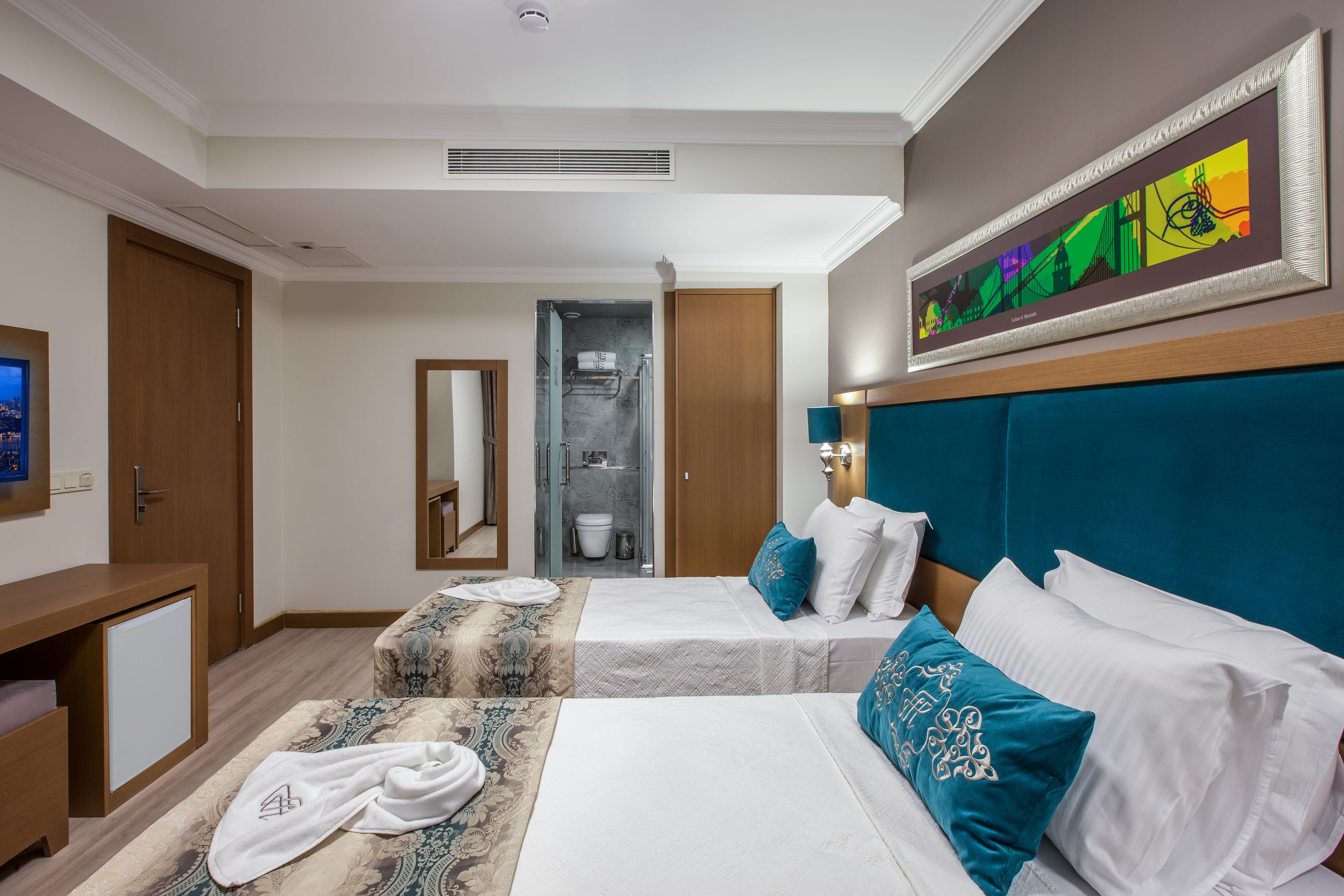 A hotel room with two beds, a bathroom, a desk, and a painting on the wall.