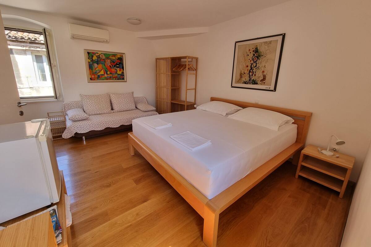 A bedroom with a wooden bed, a wooden nightstand, a wooden wardrobe, a window, and a colorful painting on the wall.