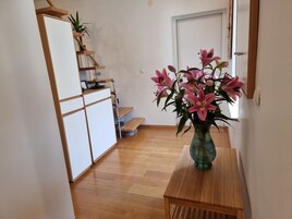A hallway with a wooden table, a vase of pink flowers, and a staircase with a plant on the landing.