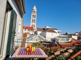Ein Balkon mit Tisch, auf dem Obst steht, und Blick auf einen historischen Turm und Gebäude.
