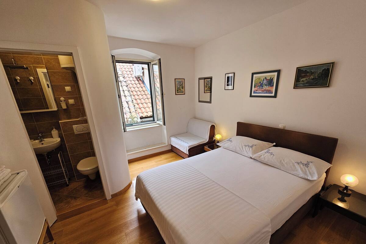 A bedroom with a large bed, a window with a view, a bedside table with a lamp, and a small seating area.