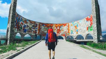 A person walking on a paved path towards a curved stone structure with colorful murals.
