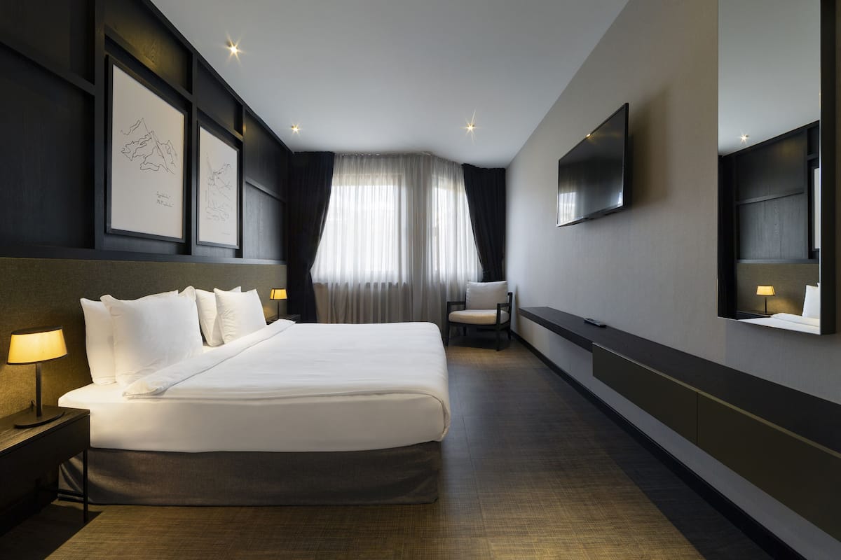 Una habitación de hotel moderna con una cama grande, un televisor de pantalla plana, un escritorio con lámpara y obras de arte enmarcadas en la pared.