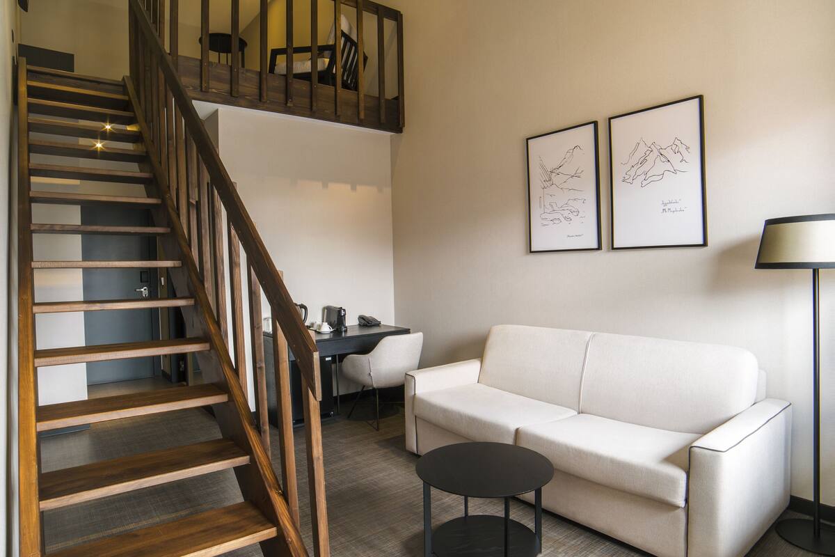 Una sala de estar moderna con una escalera de madera, un sofá blanco, una pequeña mesa redonda y dos obras de arte enmarcadas en la pared.