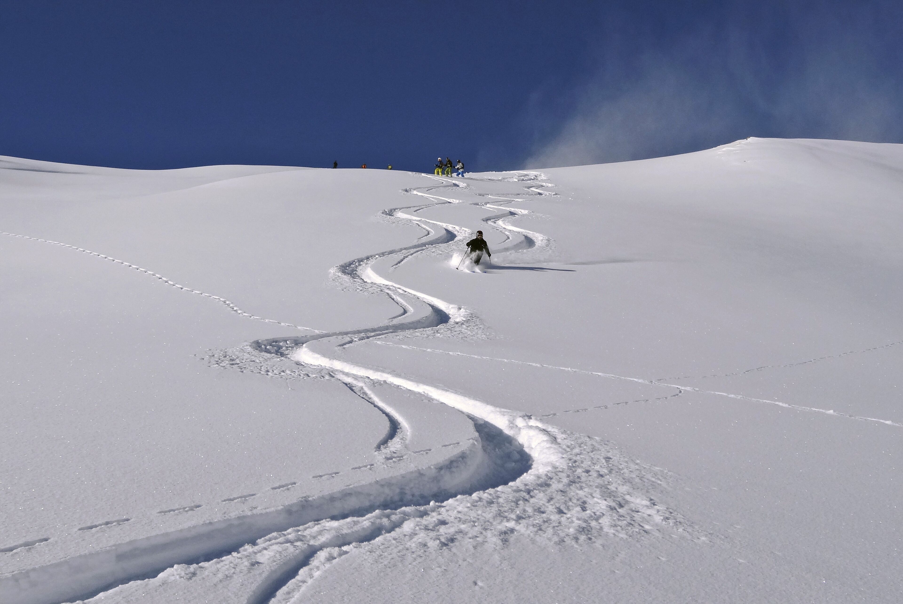 A snow-covered slope with ski tracks and a clear blue sky.