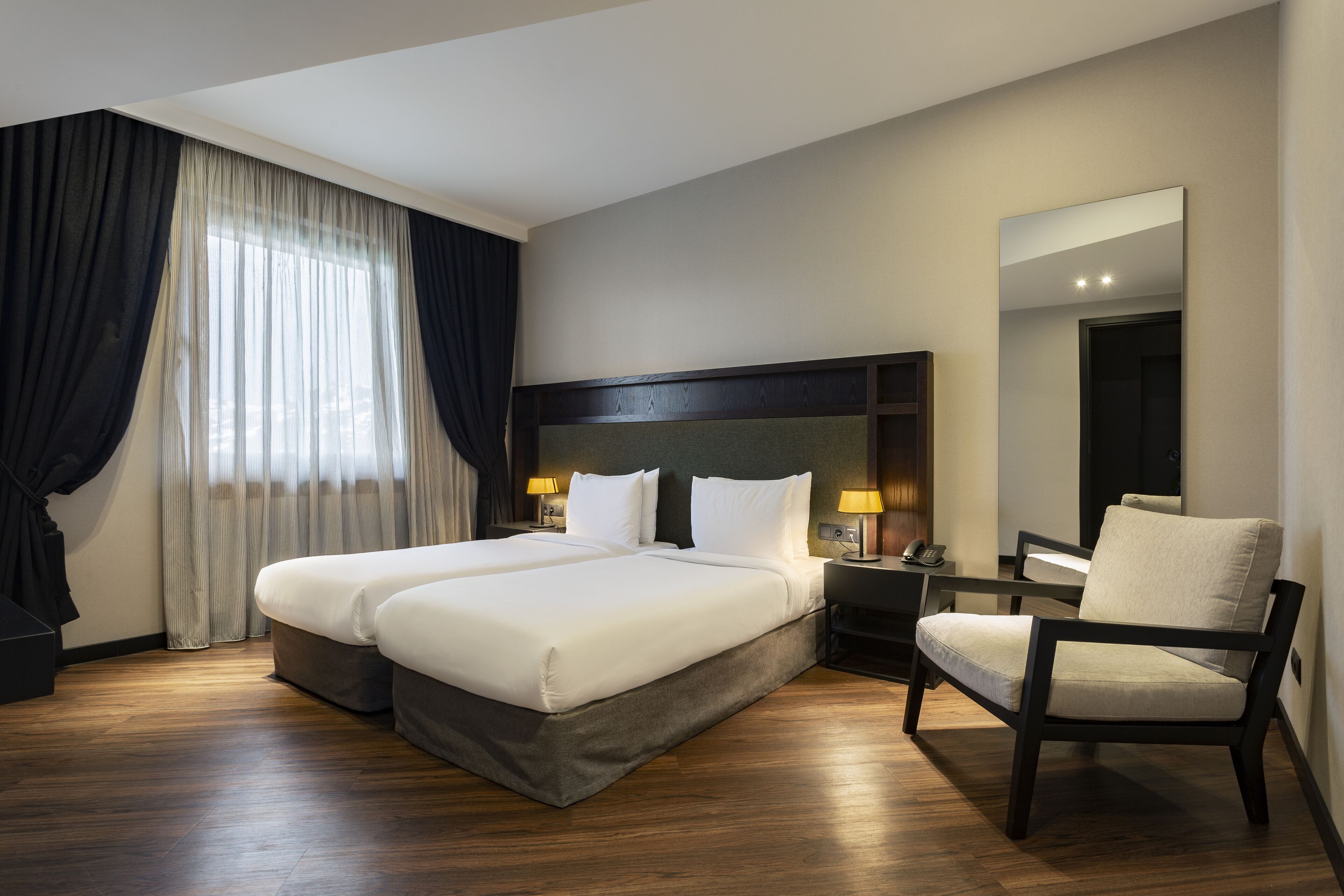 A hotel room with a large bed, a chair, a desk, and a mirror.