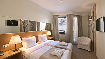A hotel room with two beds, a desk, a chair, a TV, and a window with curtains.