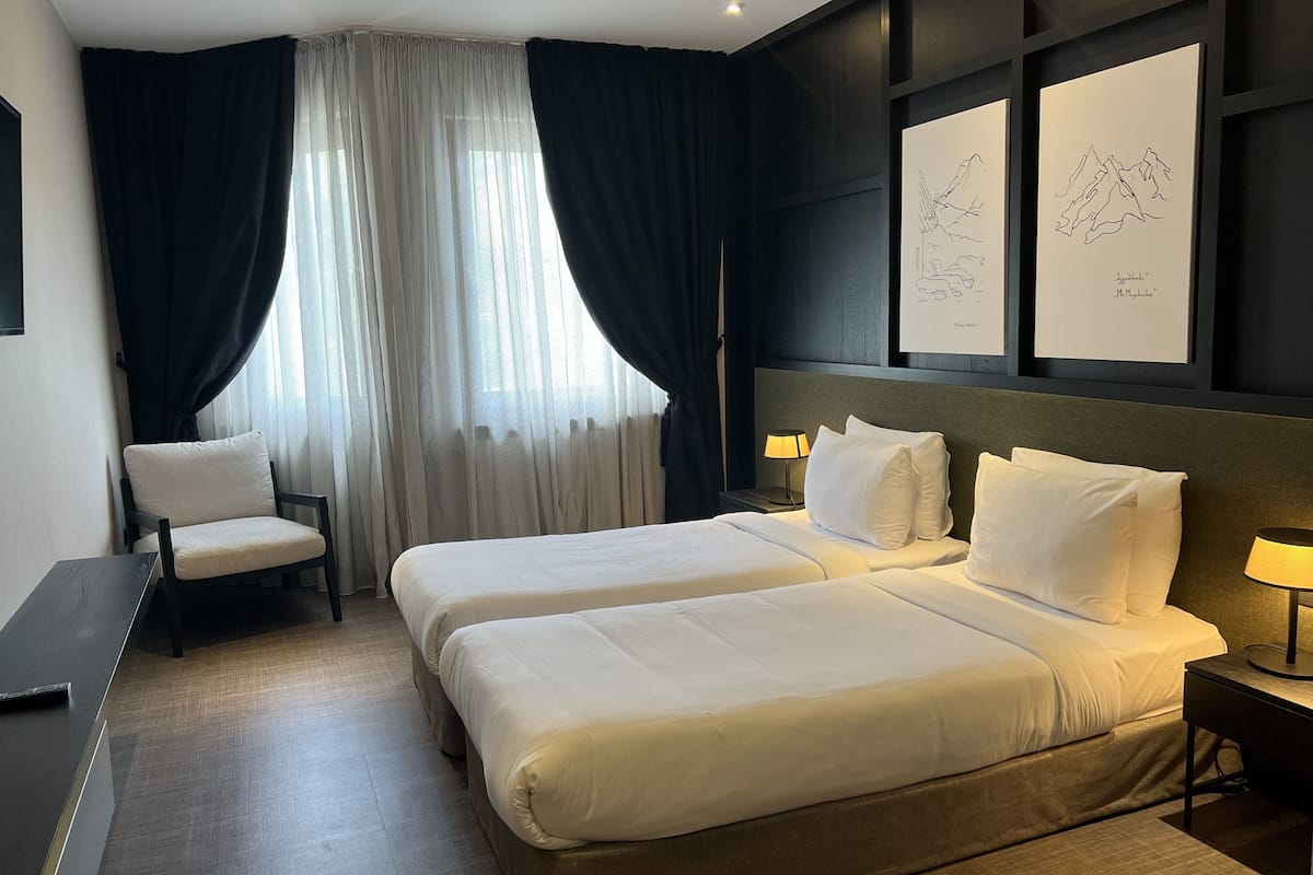 Habitación de hotel con dos camas, una silla, un escritorio y obras de arte en la pared.