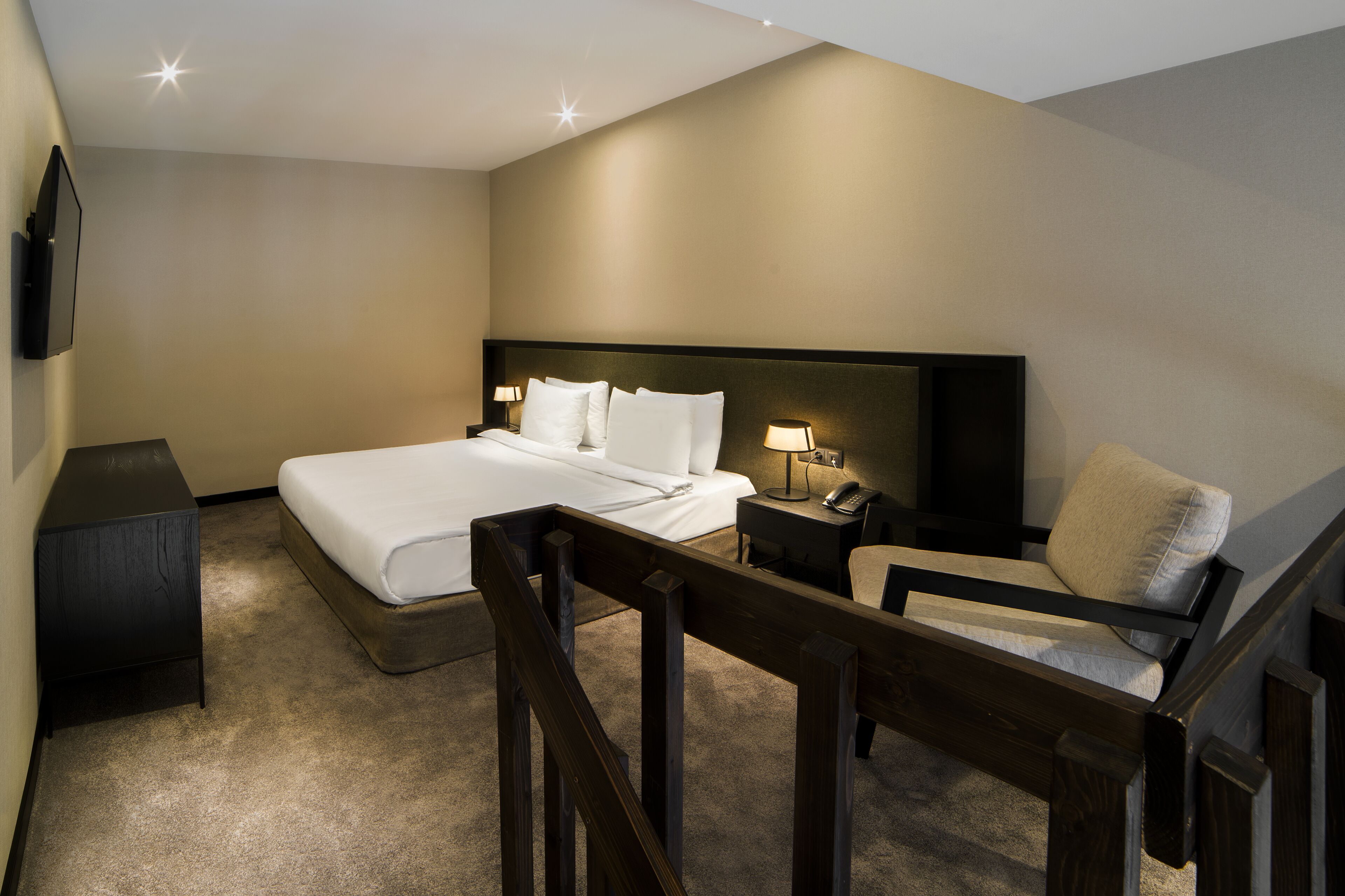 A hotel room with a large bed, bedside tables, a chair, and a TV mounted on the wall.
