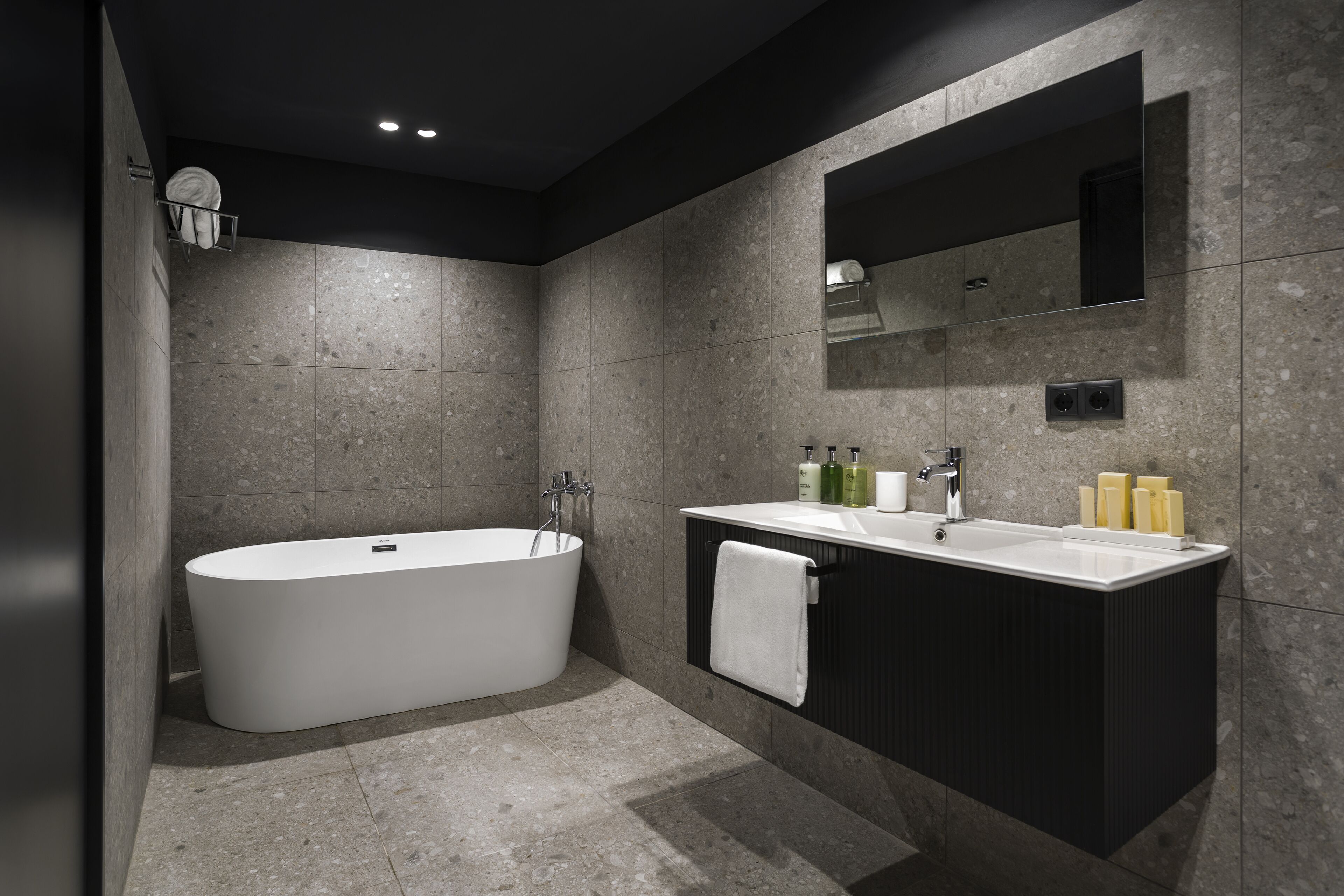 A modern bathroom with a freestanding bathtub, a vanity with a mirror, and a towel hanging on the wall.