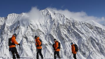 A group of climbers in orange jackets and black pants on a snowy mountain with a clear blue sky.