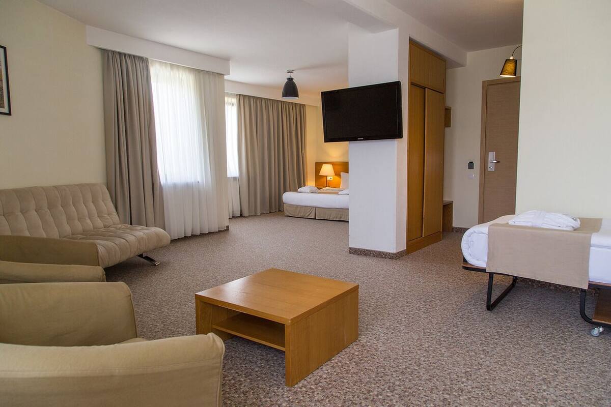 Habitación de hotel con sofá, cama, televisor montado en la pared y una mesita.
