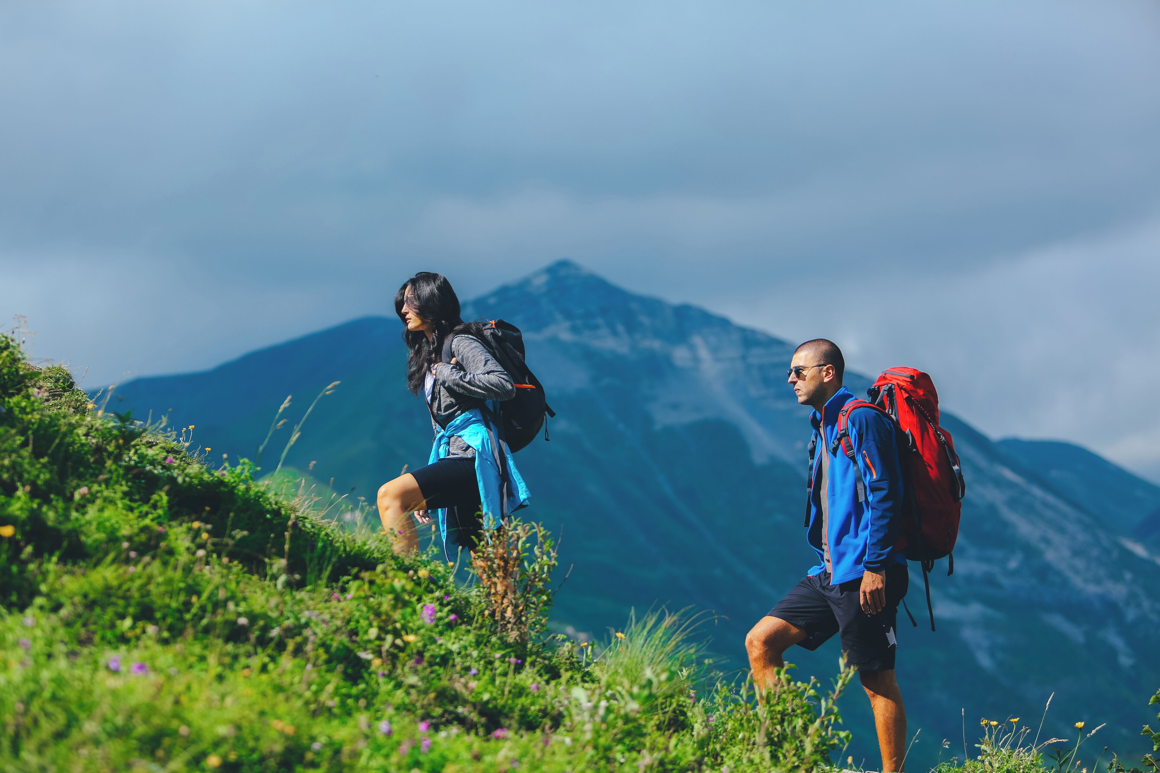 Two hikers on a mountain trail with a mountain in the background.