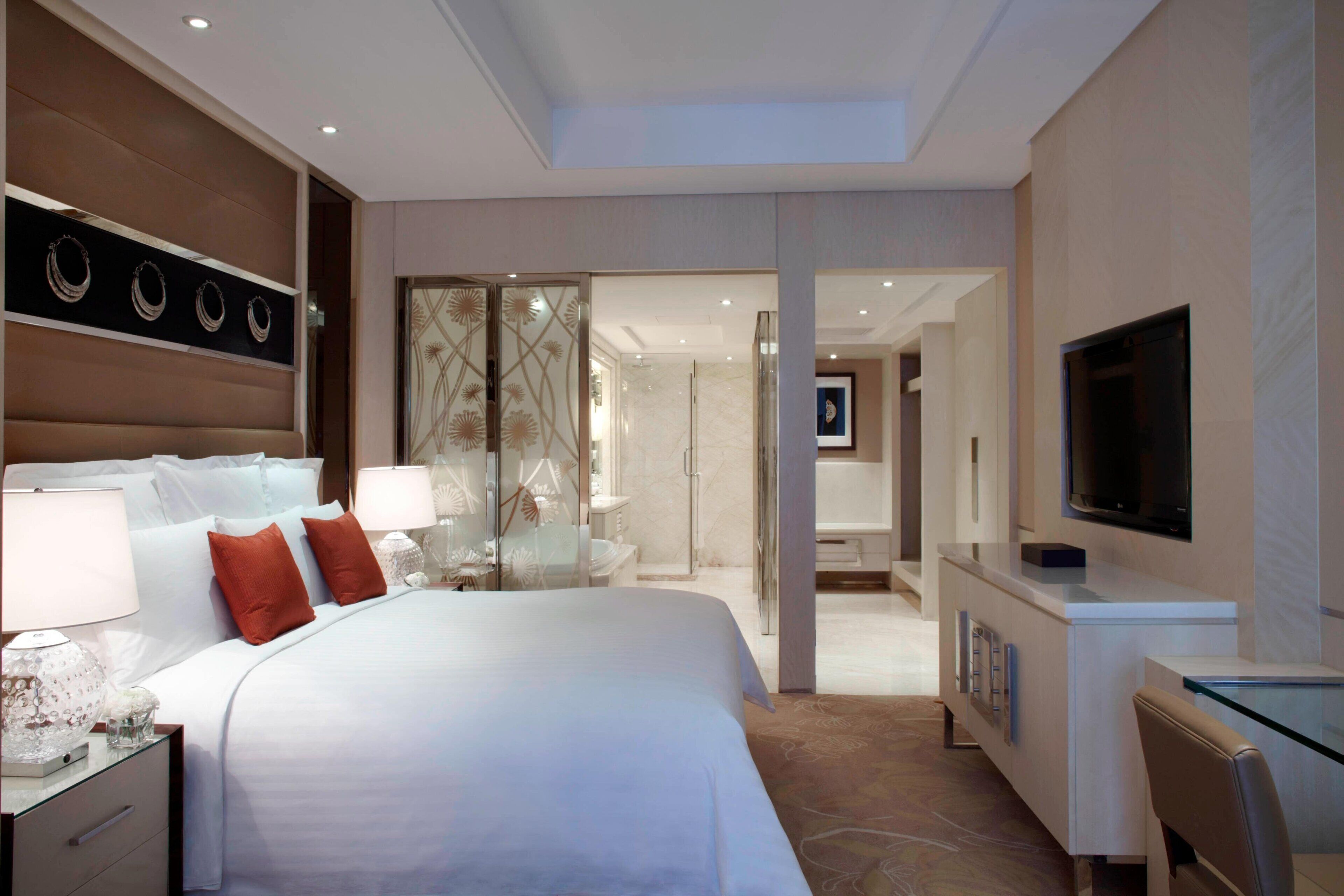 A modern hotel room with a large bed, bedside lamps, a TV, and a desk with a chair.