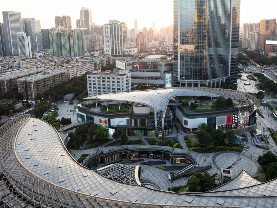 Un moderno complejo urbano con una estructura de techo curva distintiva, rodeado de edificios altos y una calle concurrida.