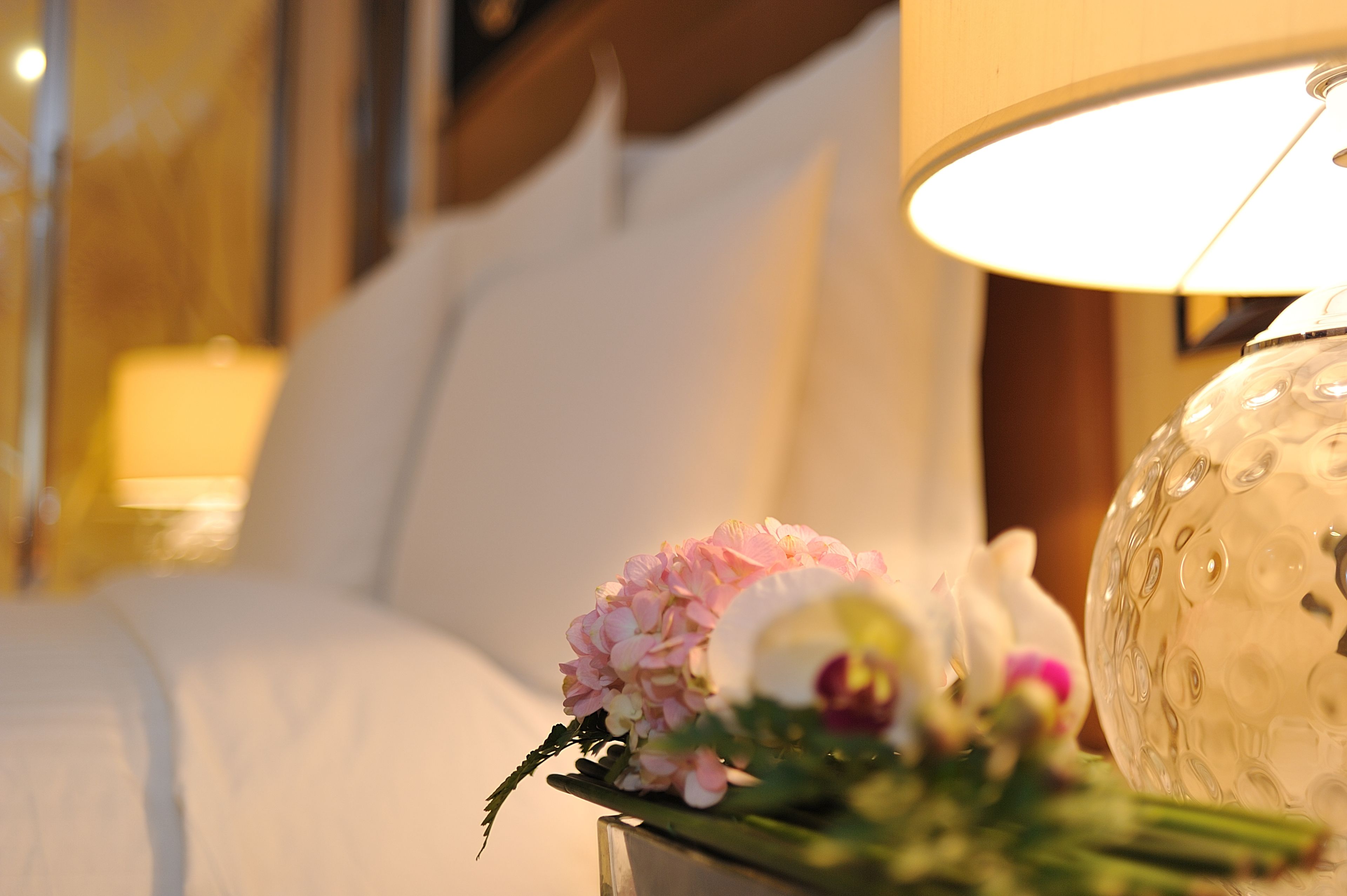 A bed with white linens, a bedside lamp, and a floral arrangement on the nightstand.