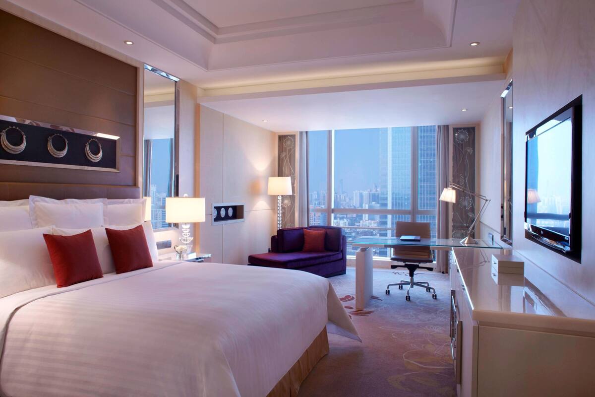 A hotel room with a large bed, a desk, a chair, and a view of the city.