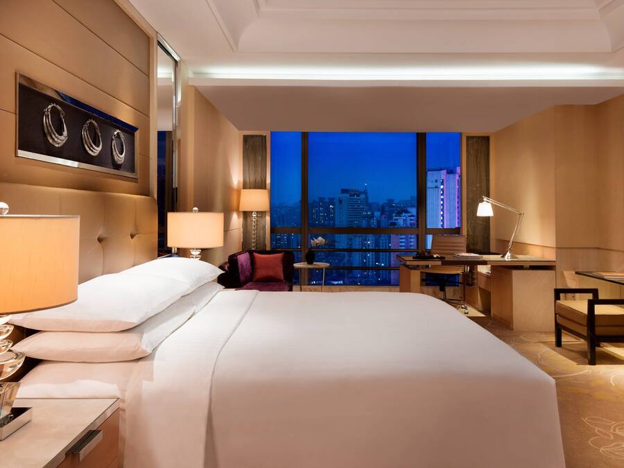 Une chambre d’hôtel moderne, dotée d’un grand lit, d’un bureau et offrant une vue sur la ville au crépuscule.