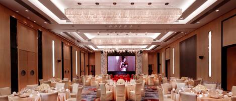 A banquet hall with round tables, chairs, and a large screen at the end.