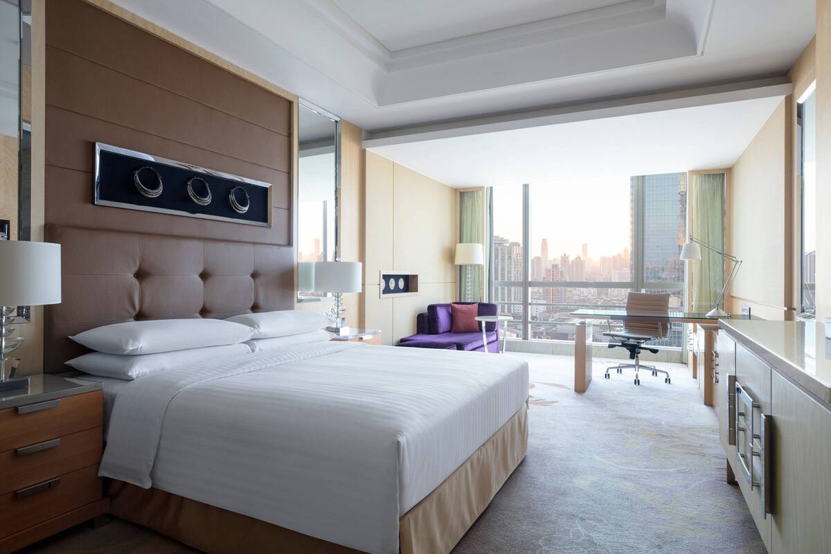 A modern hotel room with a large bed, a desk, and a view of the city.